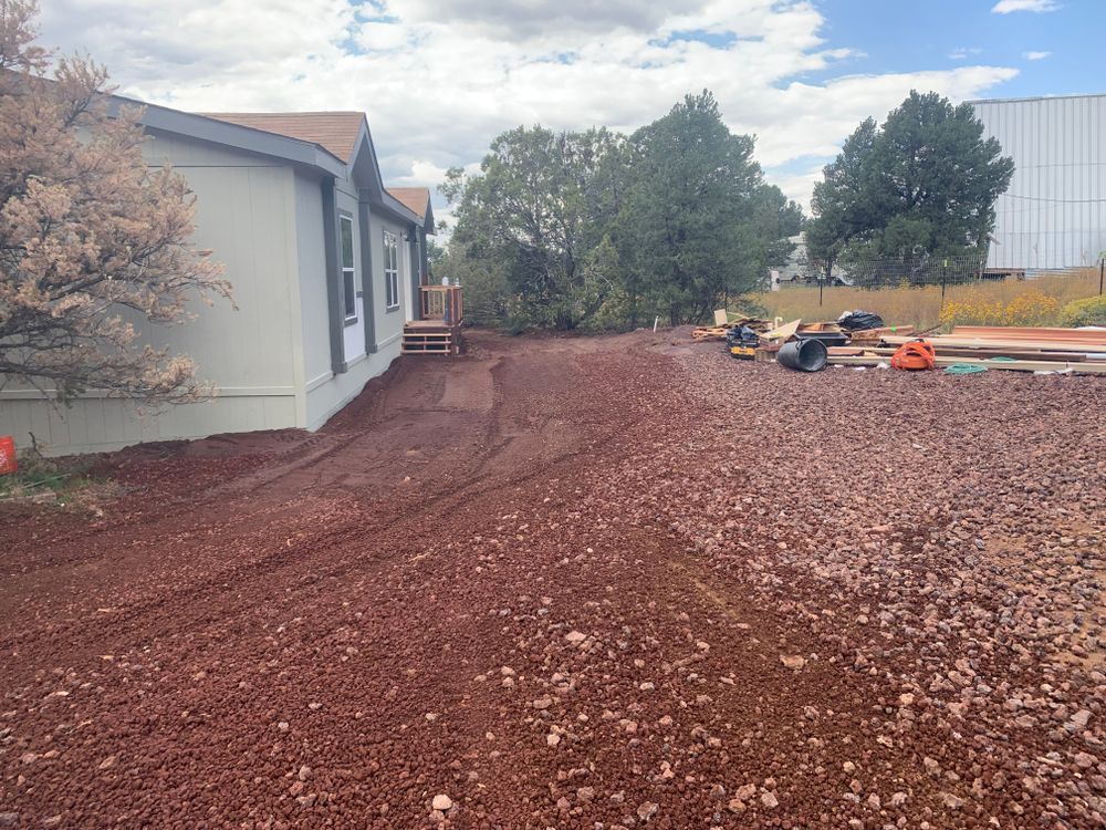 Mobile home with red gravel landscaping and construction equipment, cloudy day.