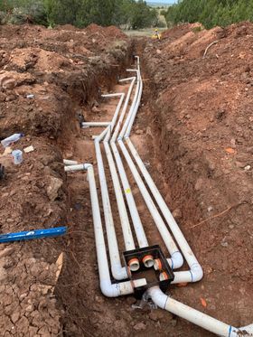 Pipes installed in a trench, likely for utilities, with multiple white PVC pipes connected to a black junction box.