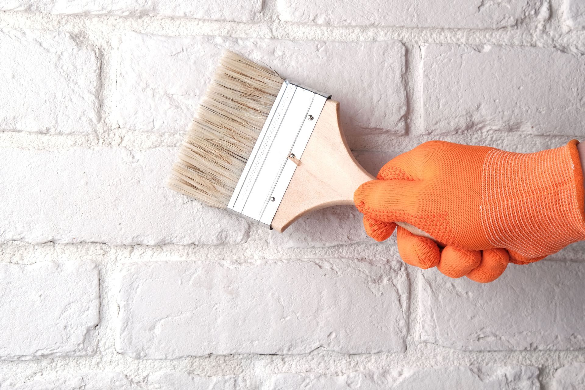 A person is painting a white brick wall with a brush.