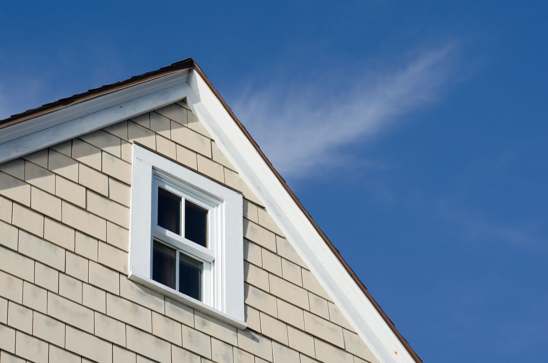 The roof of a house with a window and a blue sky in the background