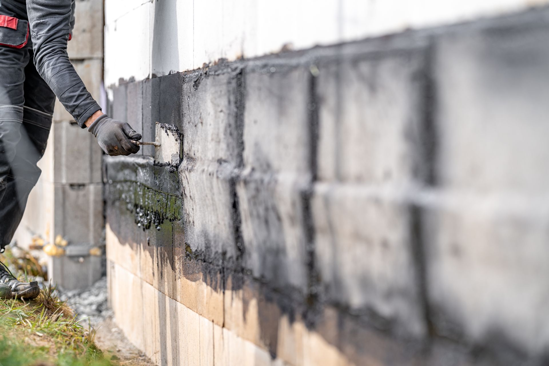 A man is painting a brick wall with black paint.