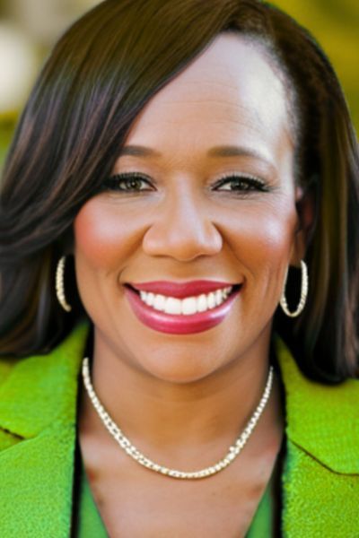 A professional headshot of author ReShonda Tate. She is a Black woman with shoulder-length, dark hair, smiling warmly at the camera. She is wearing a bright green top and subtle jewelry. The background is a soft, warm-toned outdoor  setting that puts the focus entirely on her.