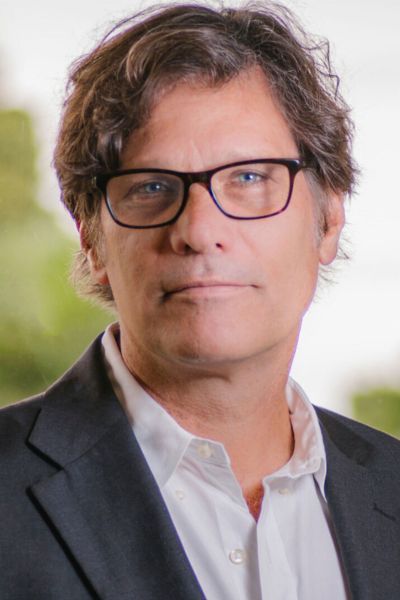 A professional headshot of author Robert Watson. He is a man with short white hair and a friendly, open expression. He is wearing a dark blue suit jacket over a crisp white dress shirt. The background is a solid, neutral gray, focusing the attention on the subject.