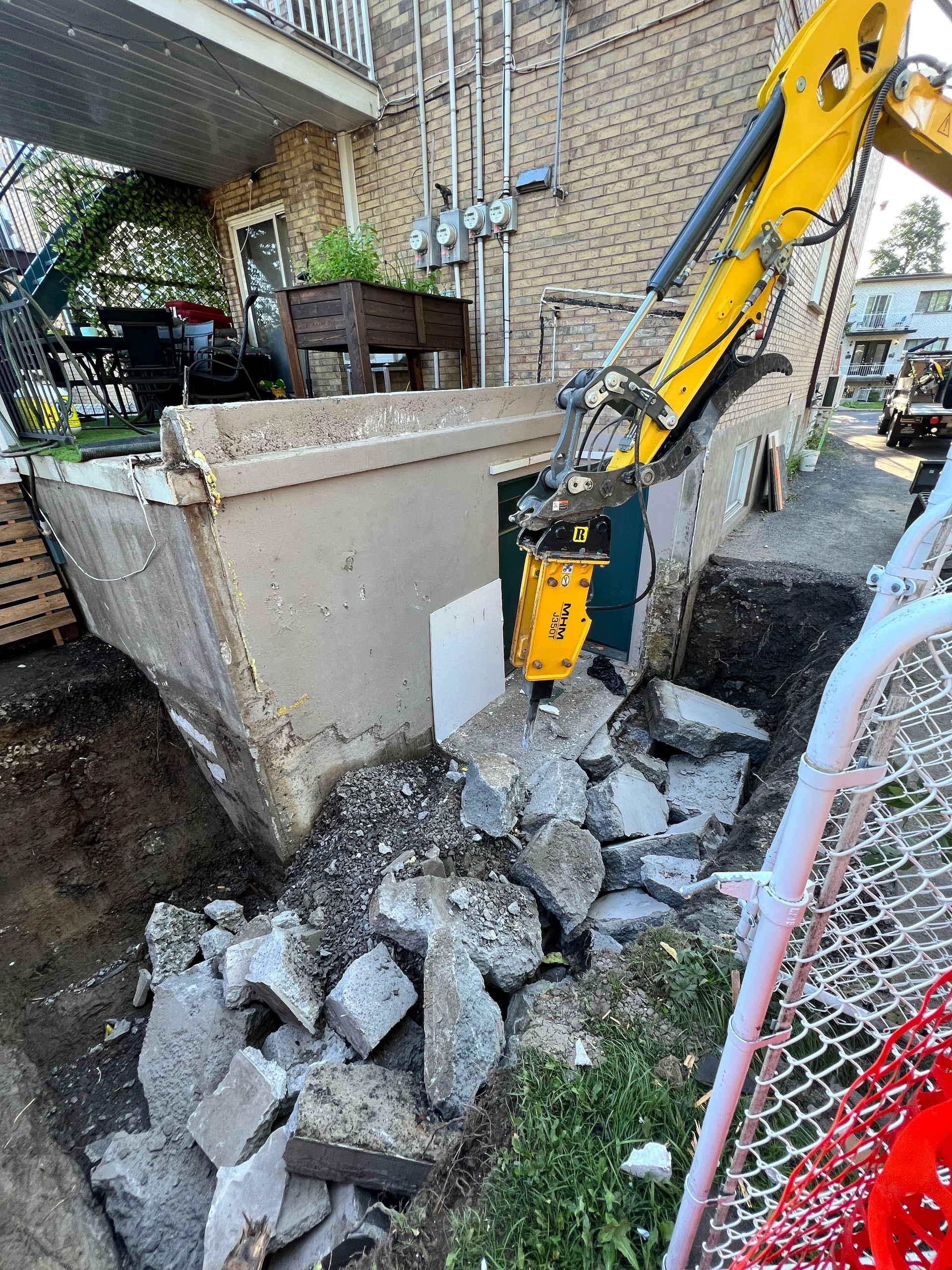 Une excavatrice jaune brise un mur de béton.
