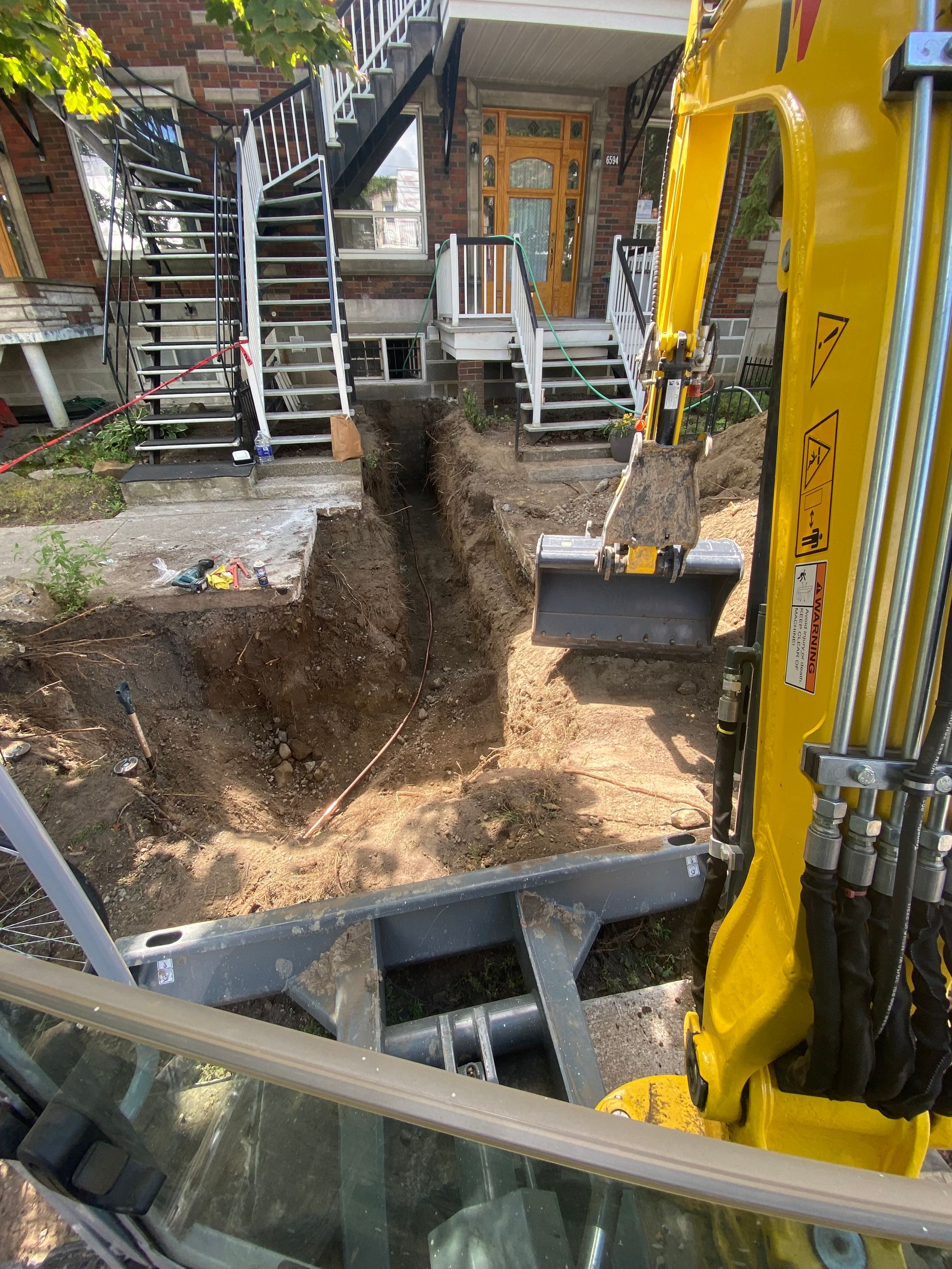 Une excavatrice jaune creuse un trou devant une maison.