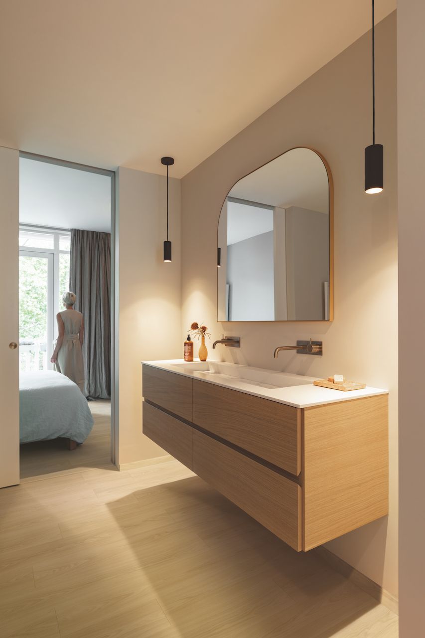 A bathroom with a sink , mirror and a door leading to a bedroom