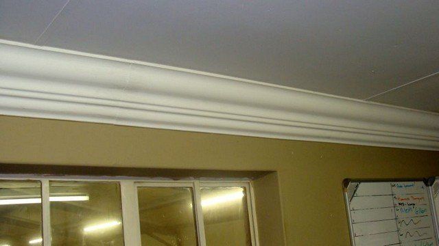 A white molding is hanging from the ceiling above a window.