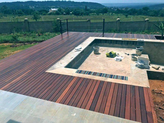 A wooden deck with a swimming pool in the background