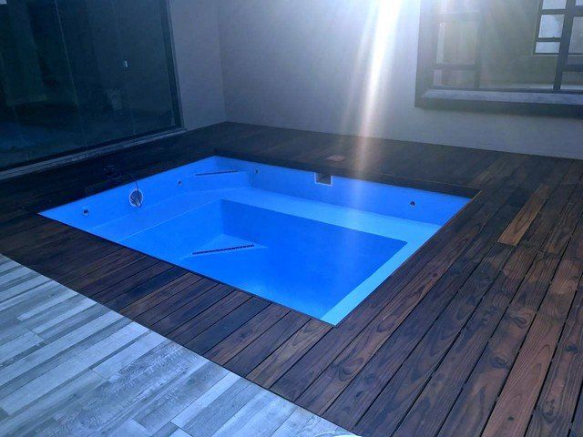 A blue swimming pool is on a wooden deck
