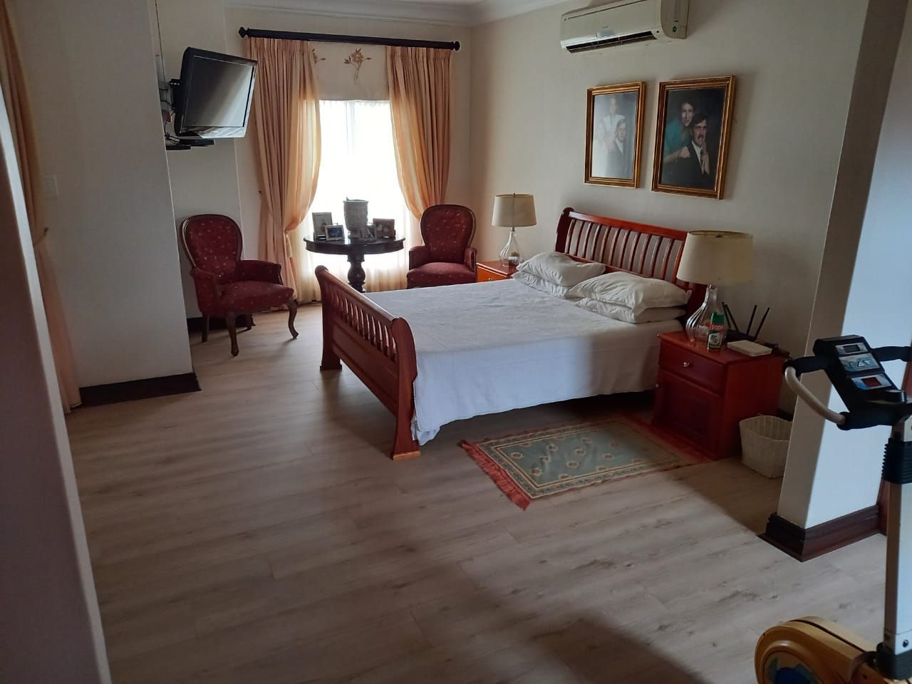 A bedroom with a bed , chairs , a treadmill and a television.