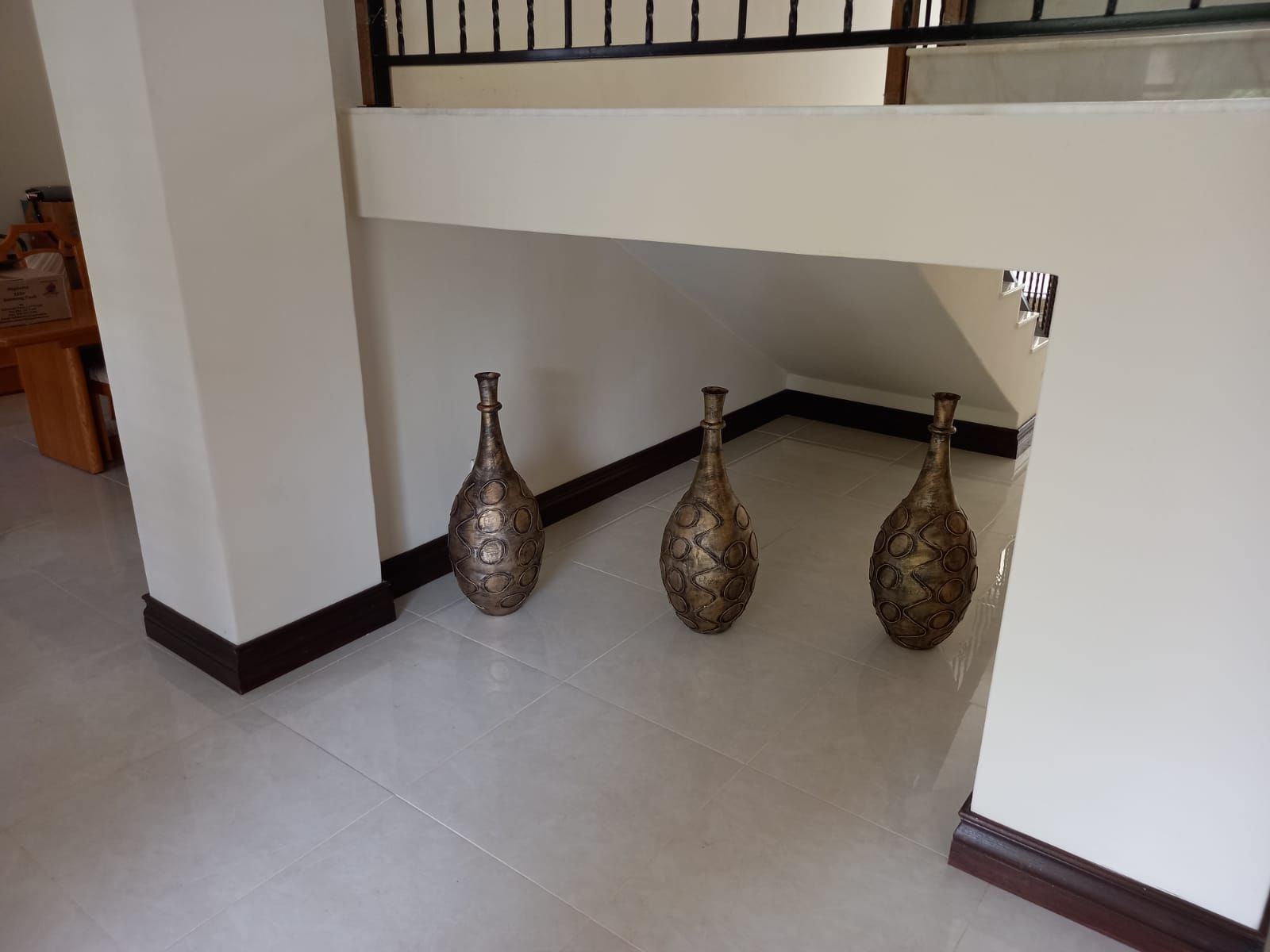 Three vases are sitting on a tiled floor under a staircase.
