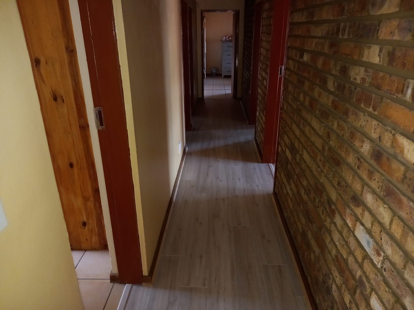 A long hallway with a brick wall and wooden doors