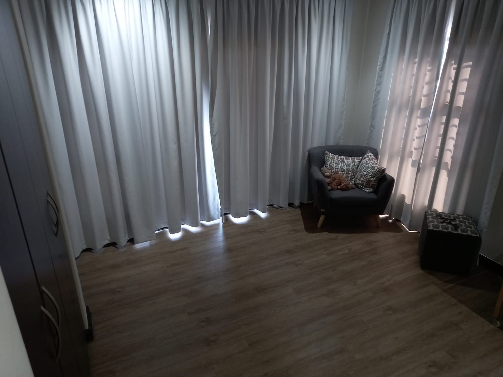 A living room with a chair and a window with white curtains.