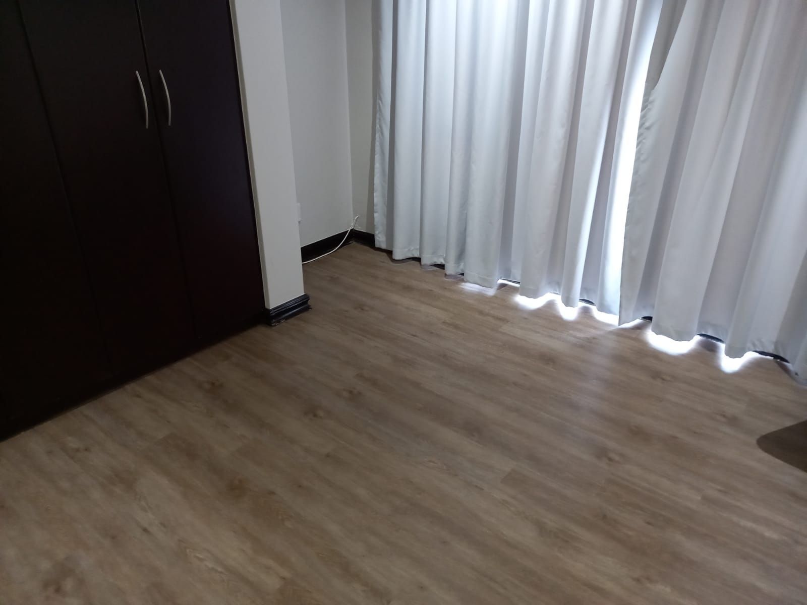 A bedroom with a wooden floor and white curtains.