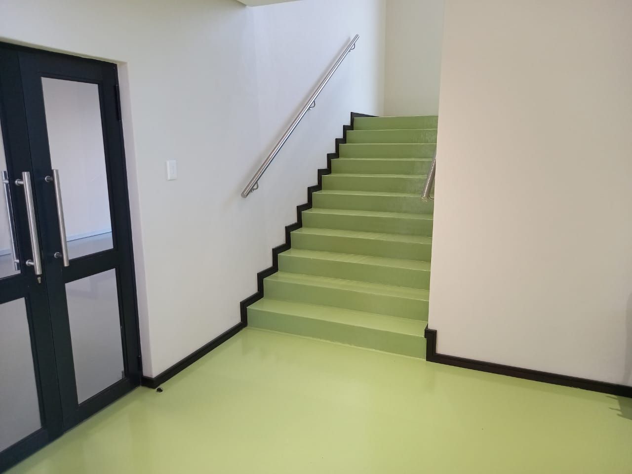 A hallway with green stairs and a black door