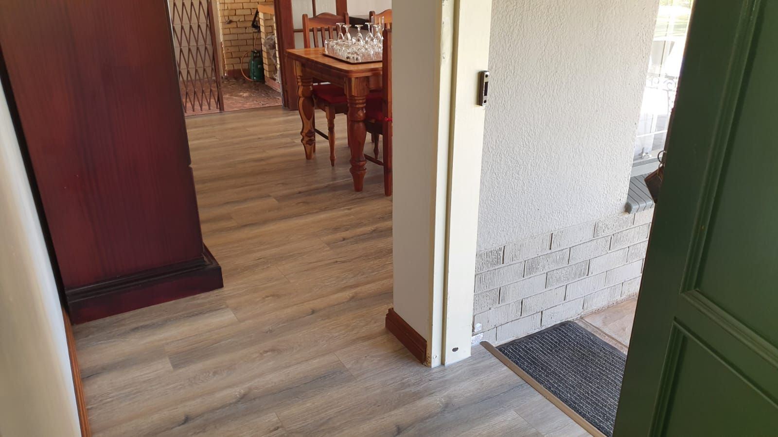 A hallway with a wooden floor and a green door leading to a dining room.