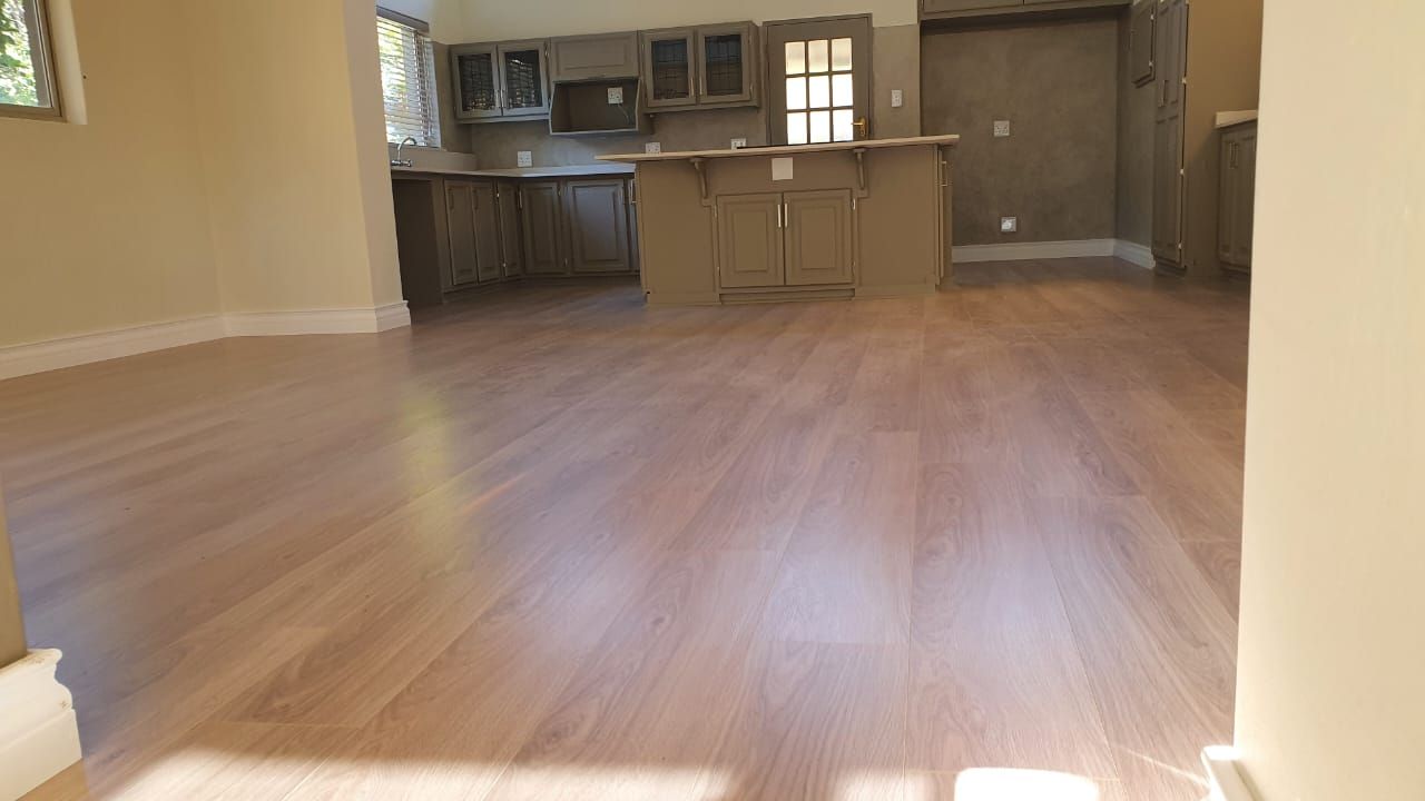 A living room with hardwood floors and a kitchen in the background.