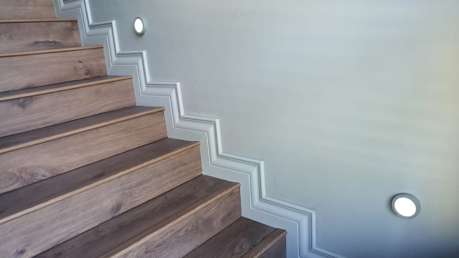 A close up of a wooden staircase with a white wall.