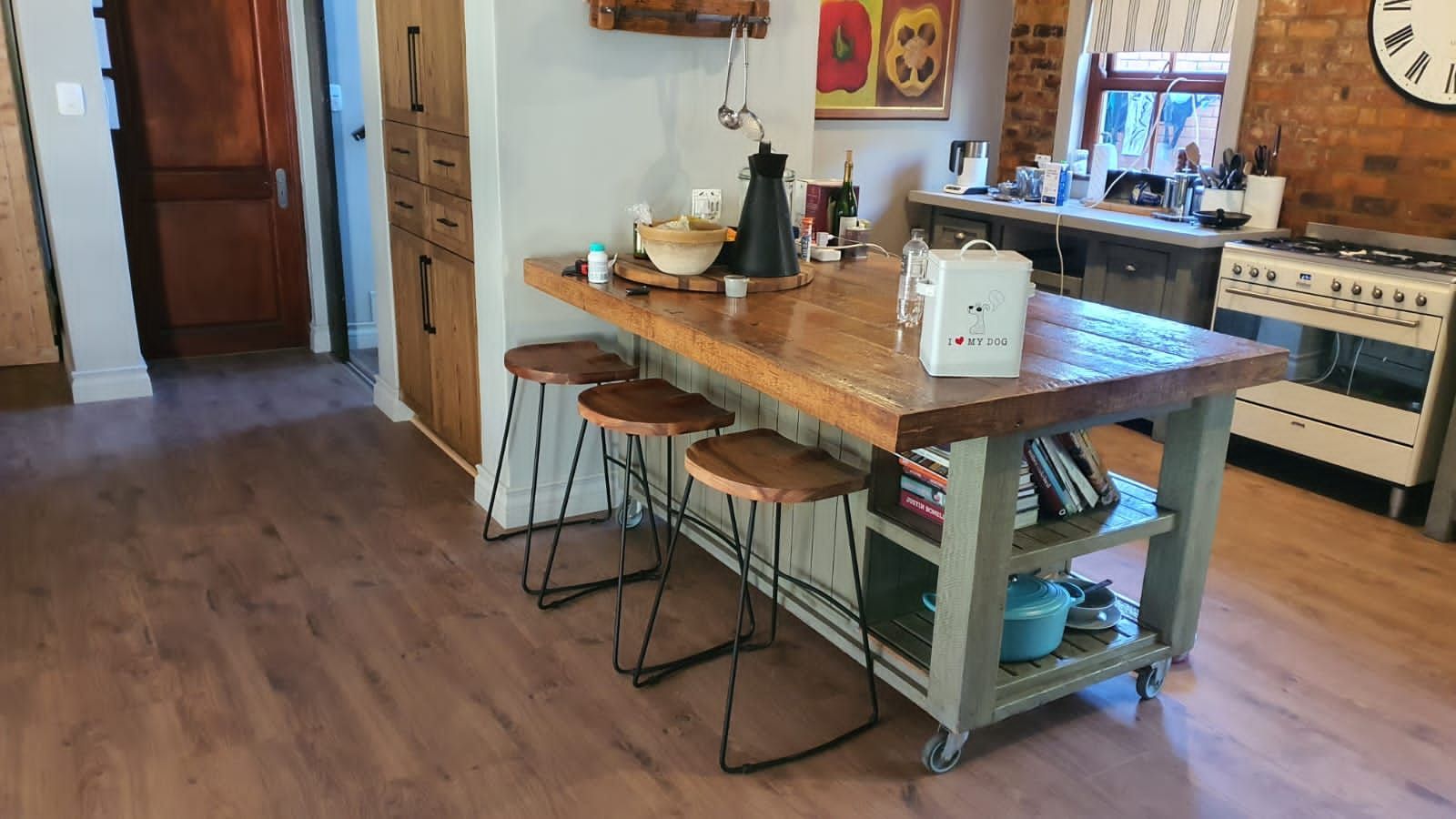 A kitchen with a large wooden table and stools and a clock on the wall.
