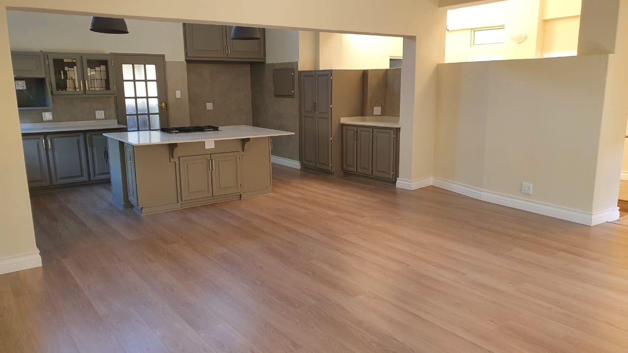 A large empty room with hardwood floors and a kitchen in the background.