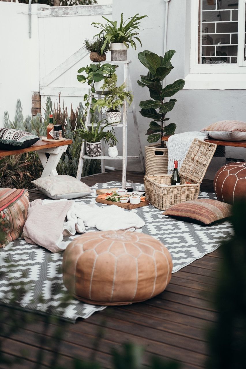 A wooden deck with a rug , ottomans , pillows and plants.