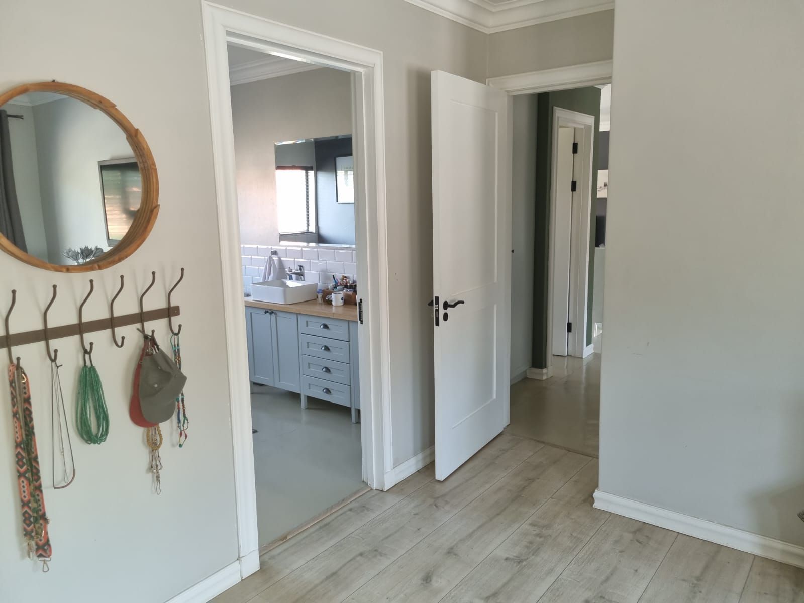 A hallway in a house with a mirror and hooks on the wall.