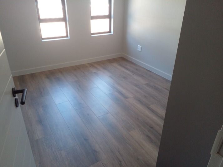 An empty room with a wooden floor and two windows