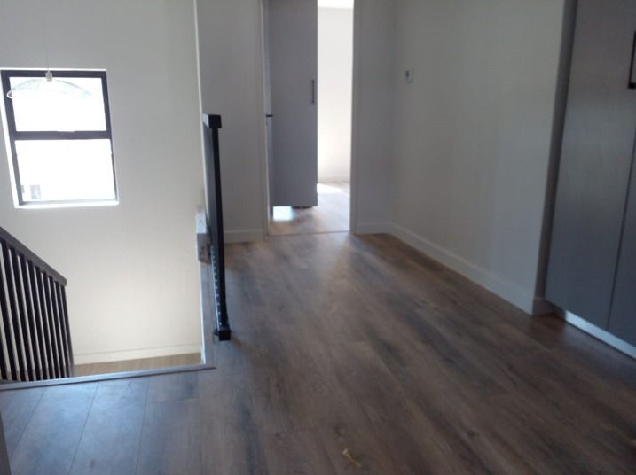 A hallway with wooden floors and stairs in a house.