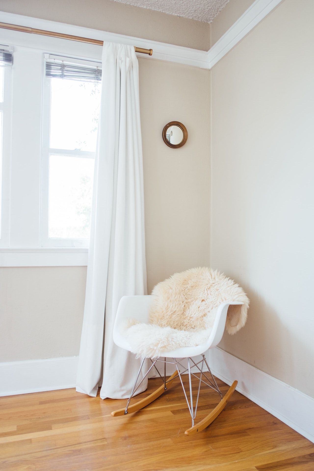 A white rocking chair is sitting in a corner of a room next to a window.