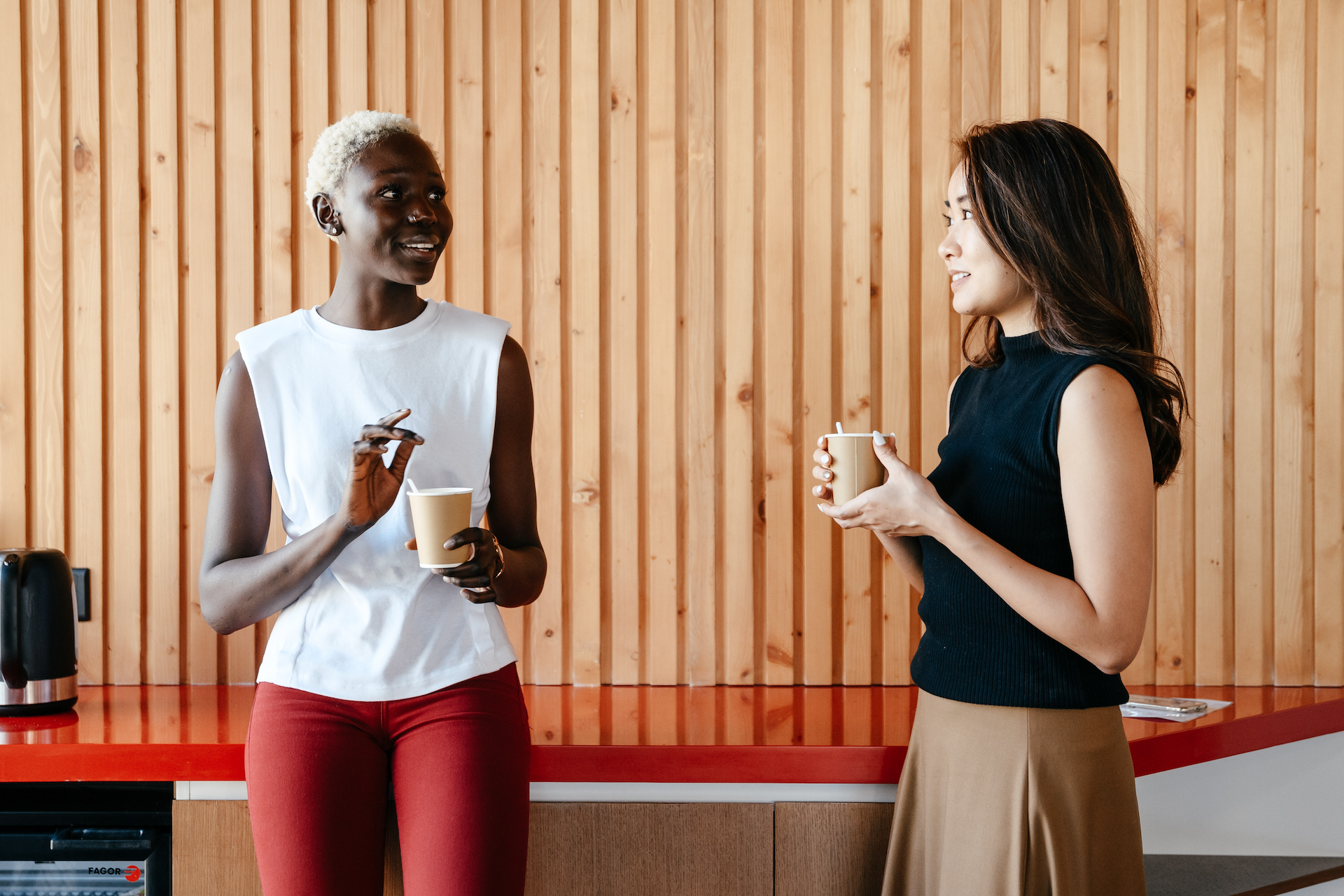 Two women are standing next to each other holding cups of coffee.