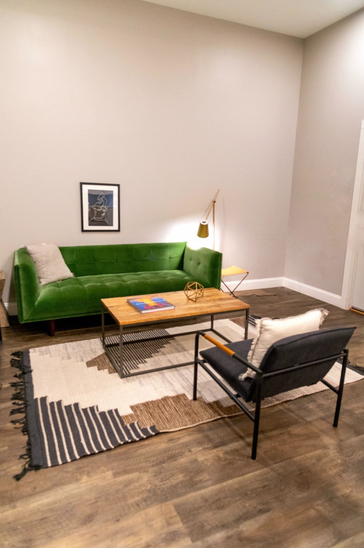 A living room with a green couch , chair , coffee table and rug.