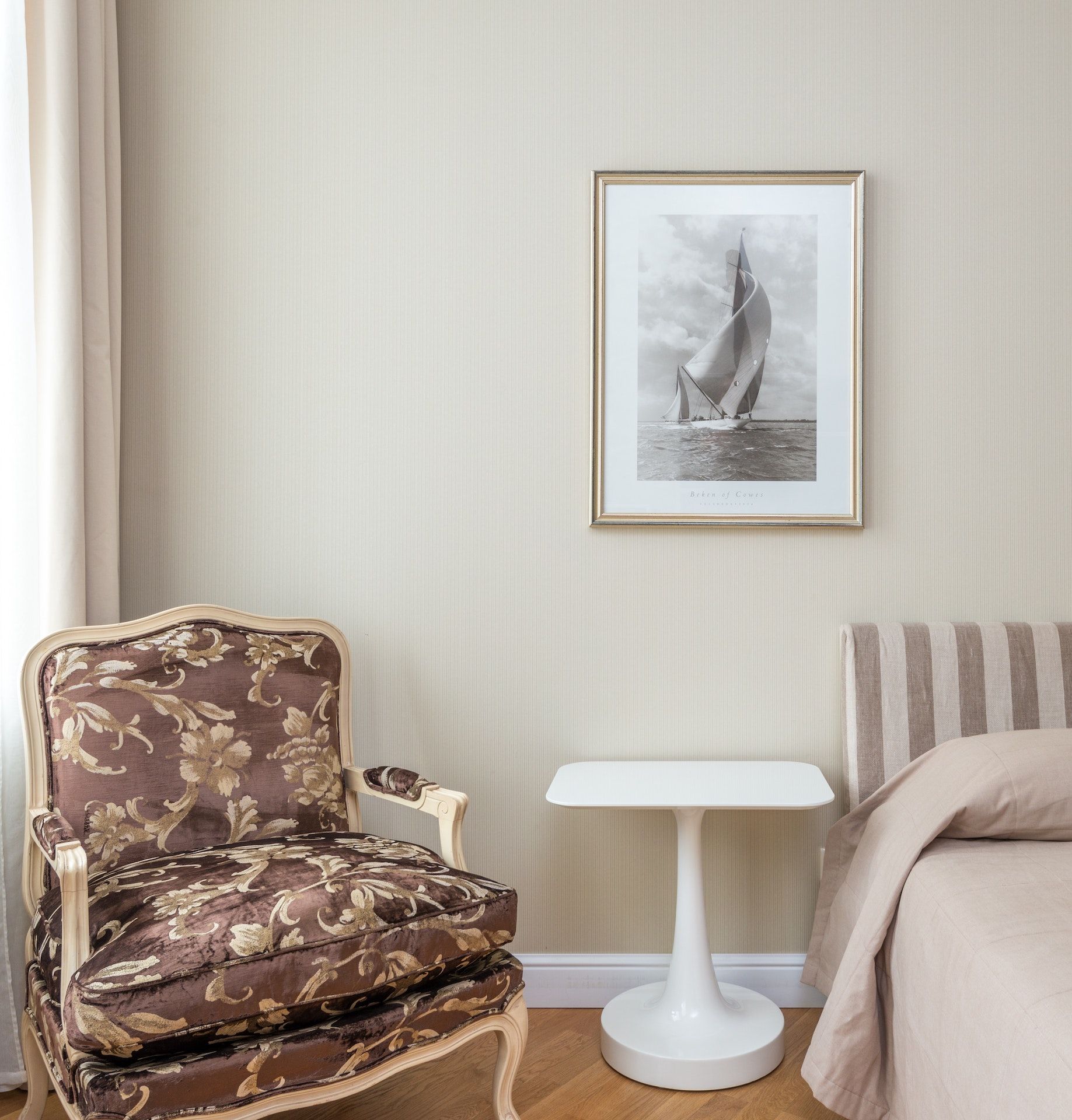 A picture of a sailboat hangs above a chair in a bedroom