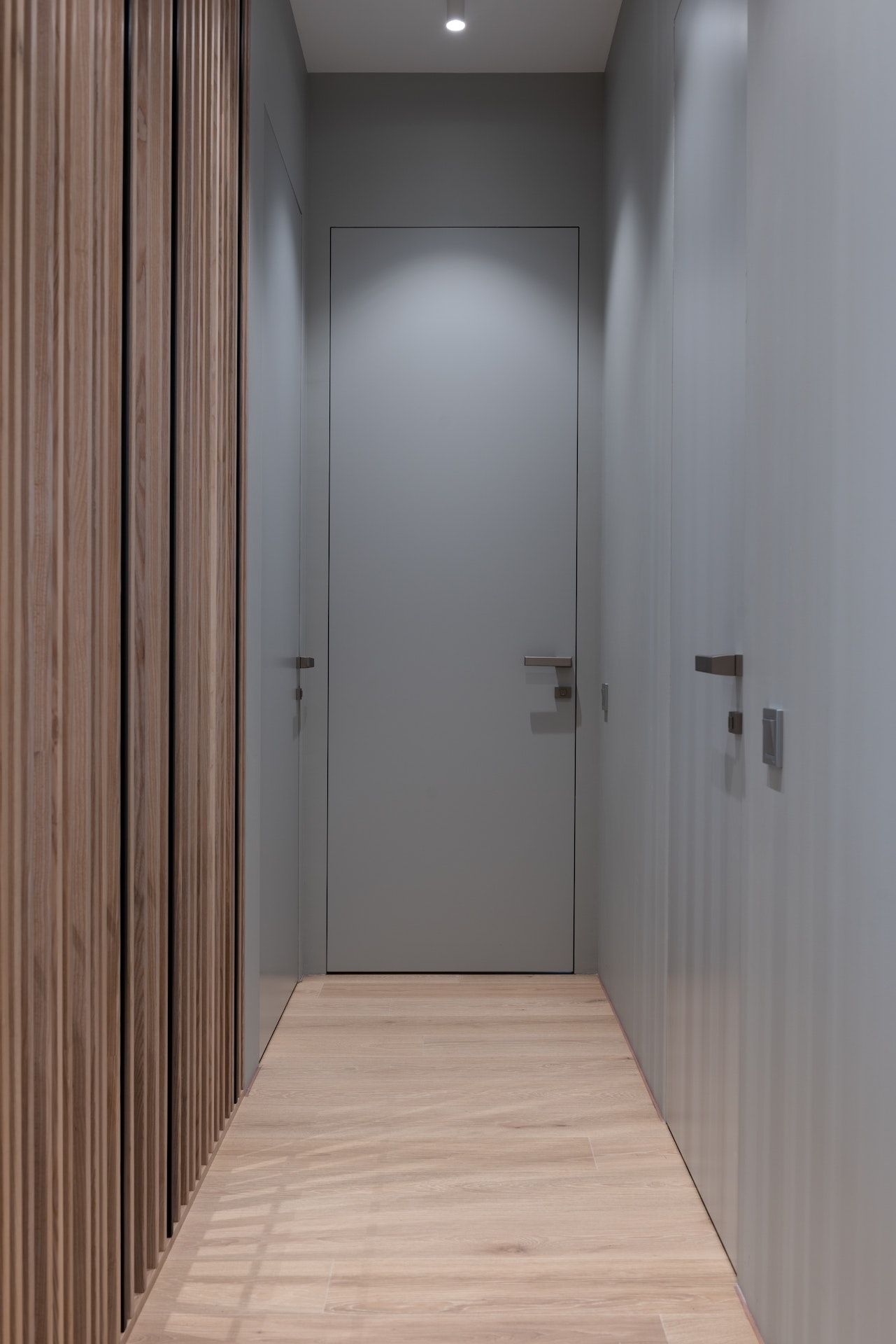 A long hallway with a gray door and wooden floors.