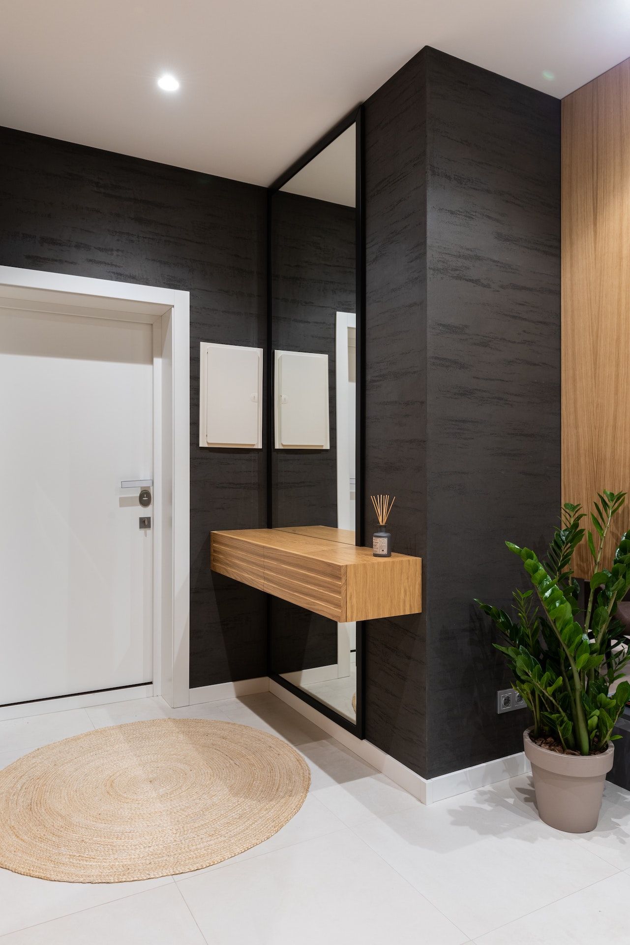 A hallway with black walls , a wooden shelf and a mirror.