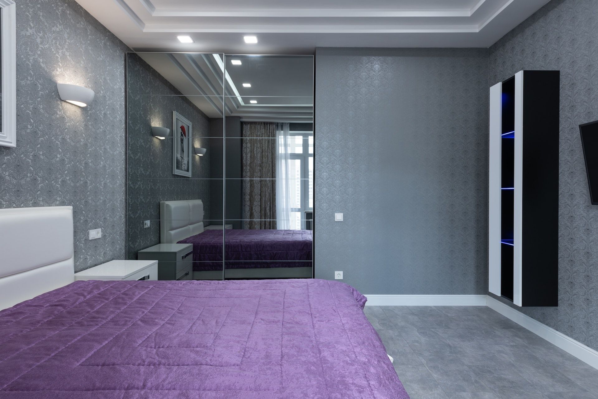 A bedroom with a purple blanket and a large mirrored wardrobe.
