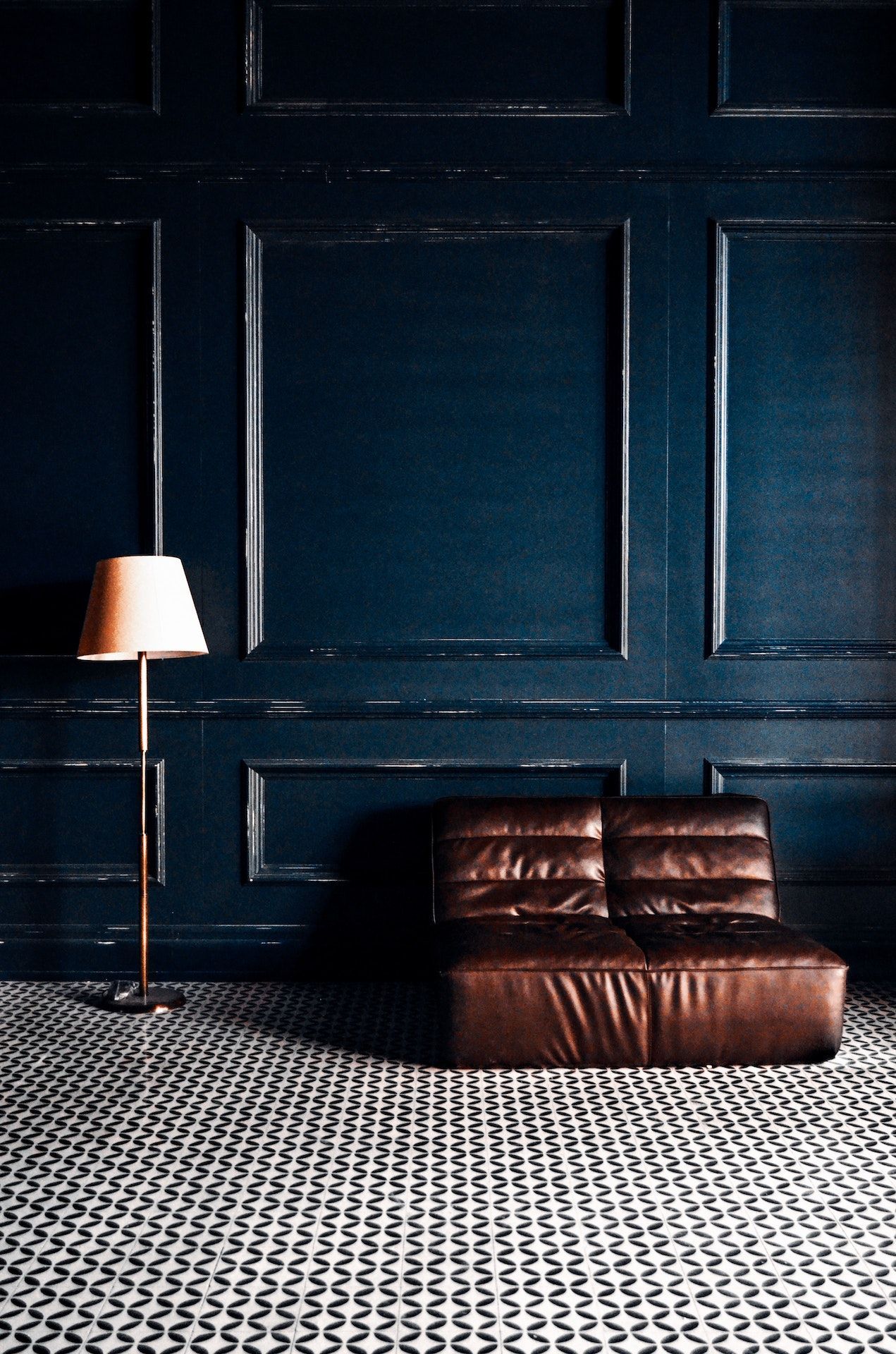 A brown leather couch is sitting in a dark room next to a lamp.