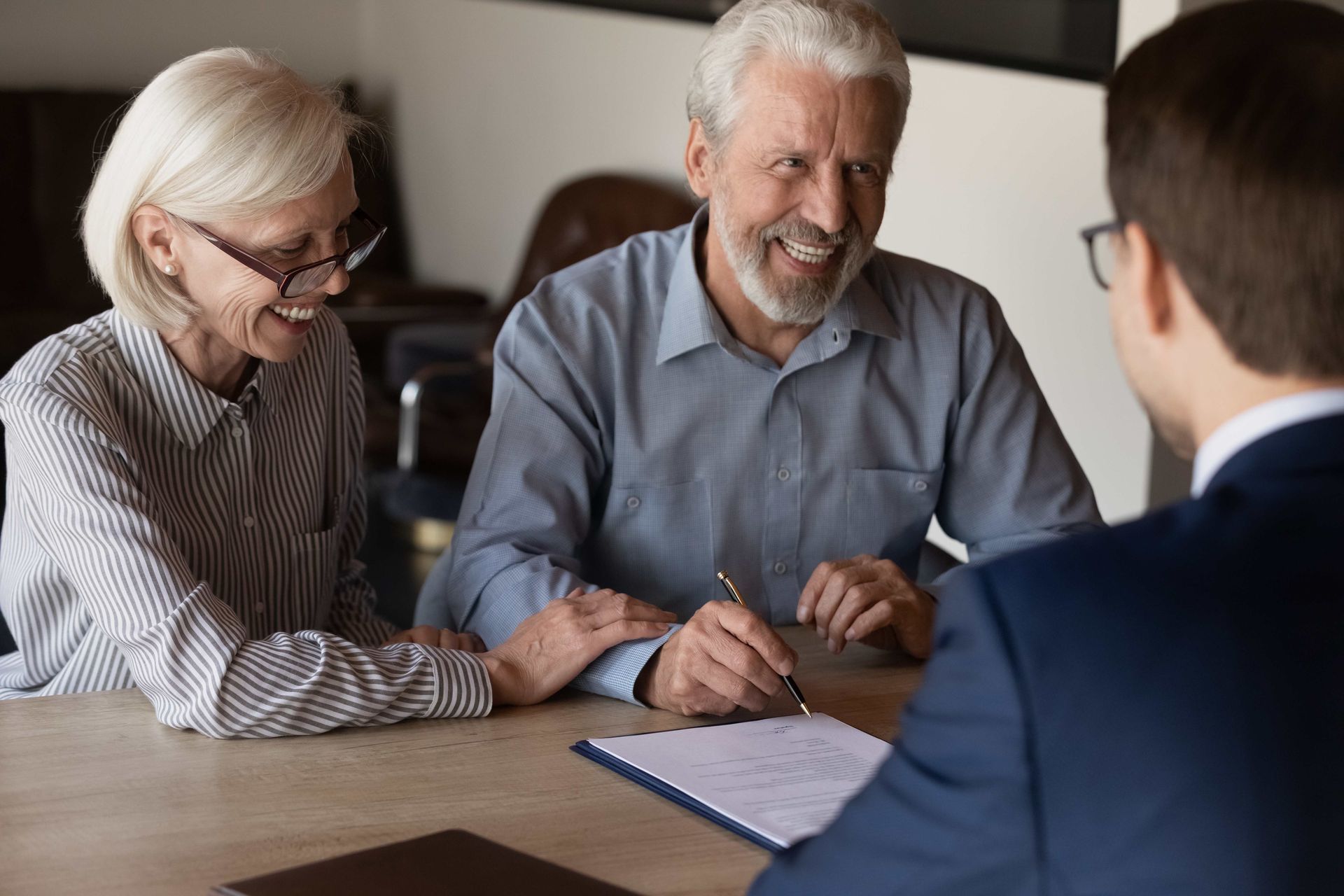 an elderly couple is sitting at a table talking to a man in a suit