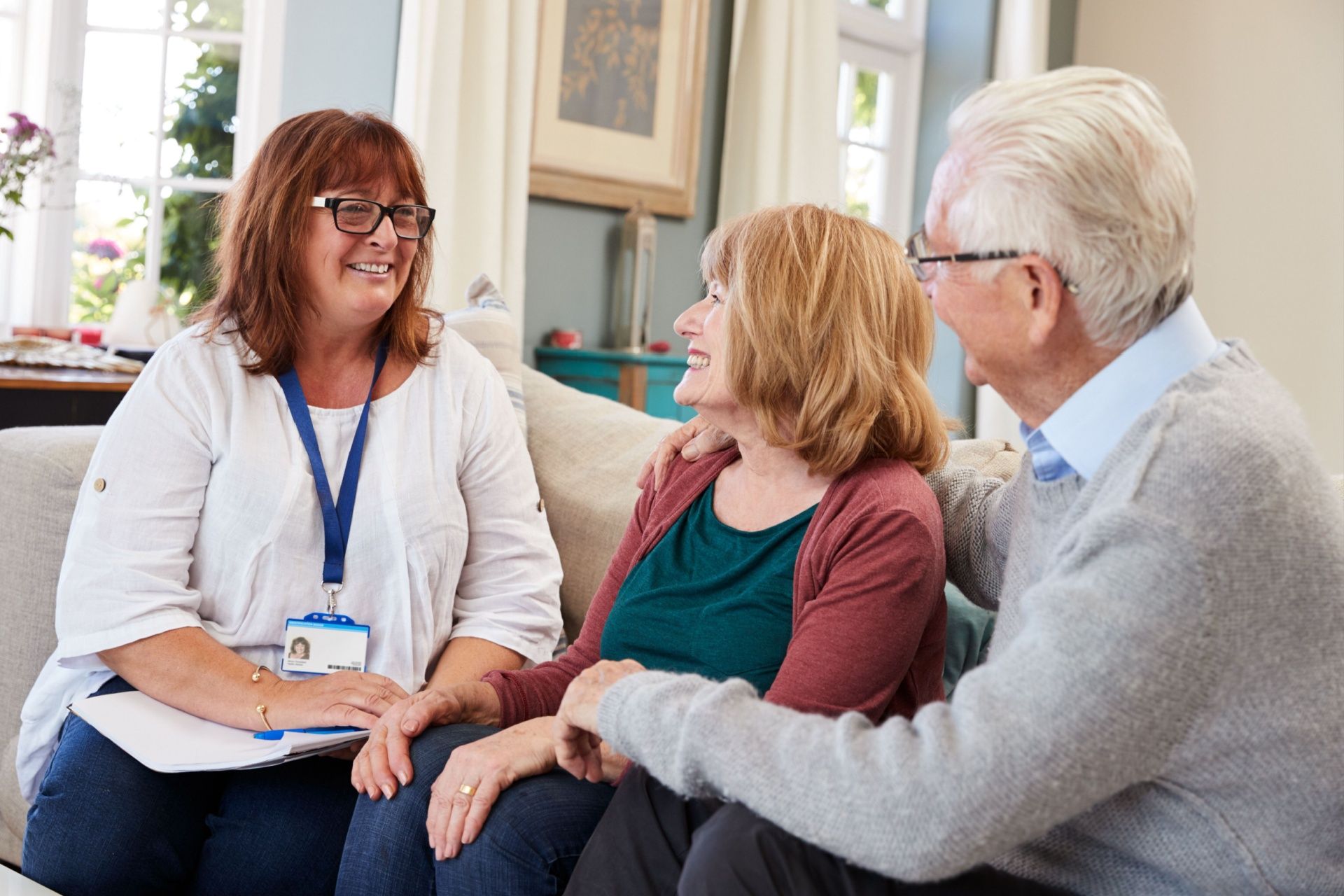 A woman is sitting on a couch talking to an elderly couple.