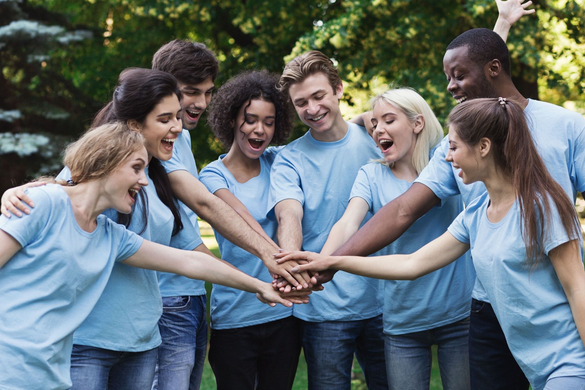 A group of young people are putting their hands together in a park.