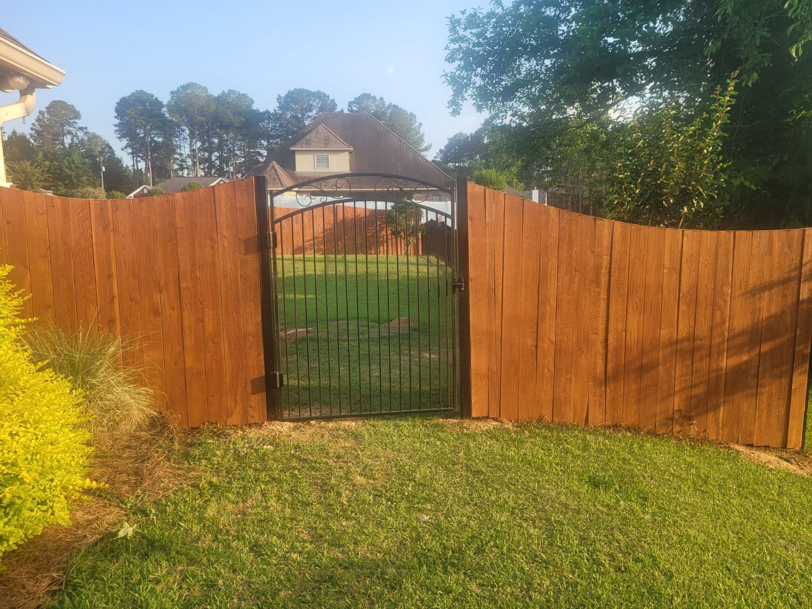 A wooden fence with a metal gate leading to a yard.