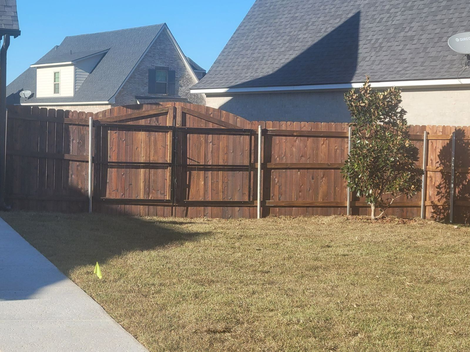 A wooden fence surrounds a grassy yard in front of a house