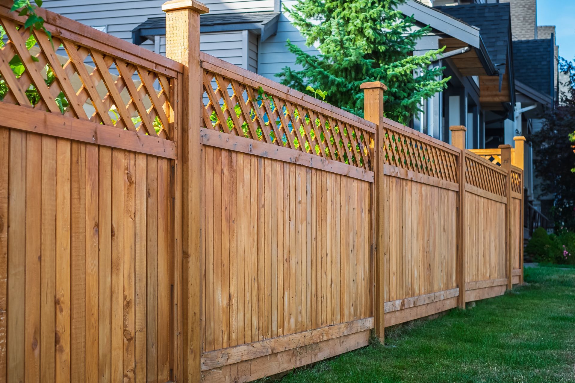 Wooden fence with lattice top, surrounding a green yard, in front of houses.