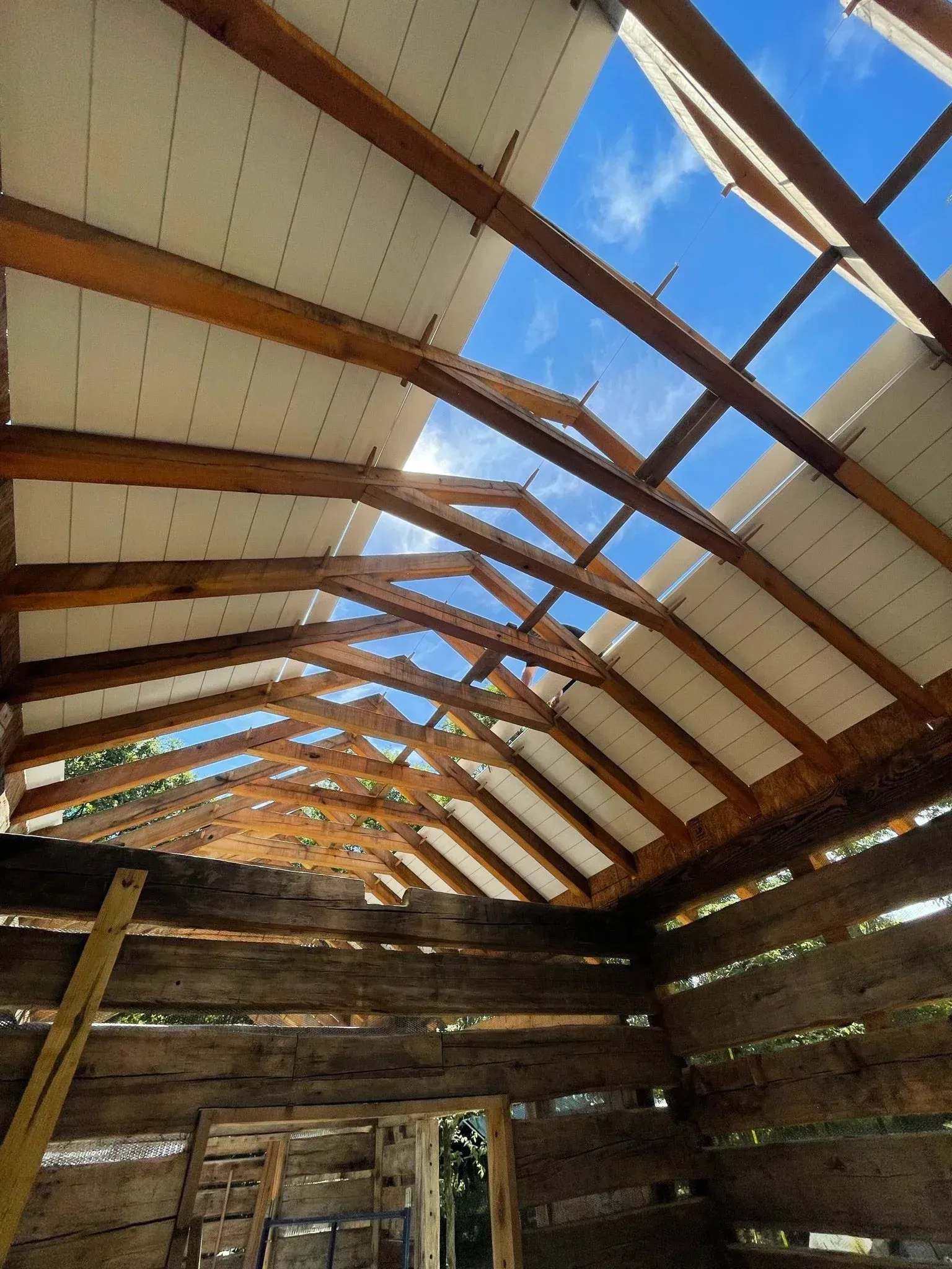 Damaged wooden roof with exposed rafters and holes, showing blue sky overhead