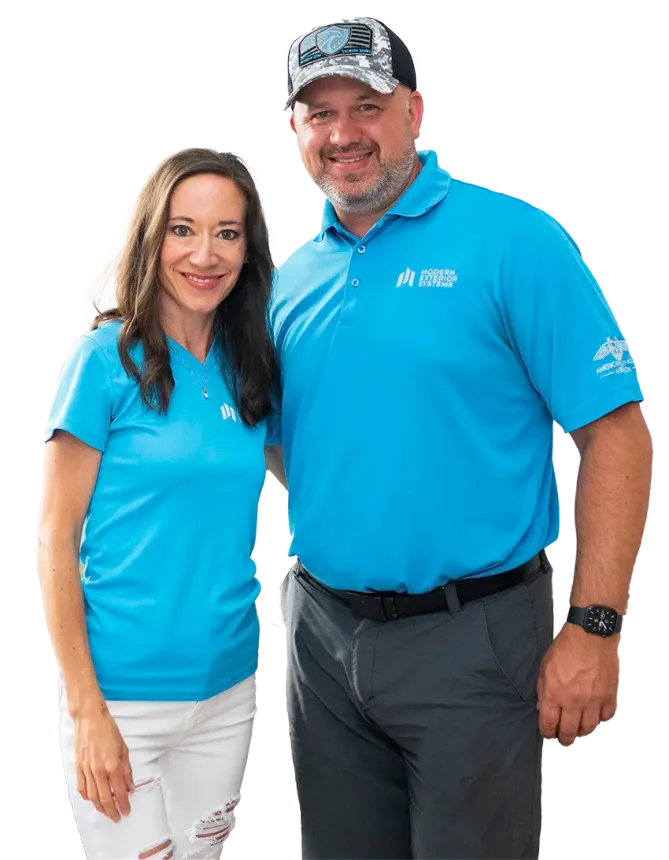 Woman and man smiling, wearing matching light blue shirts, standing close together.