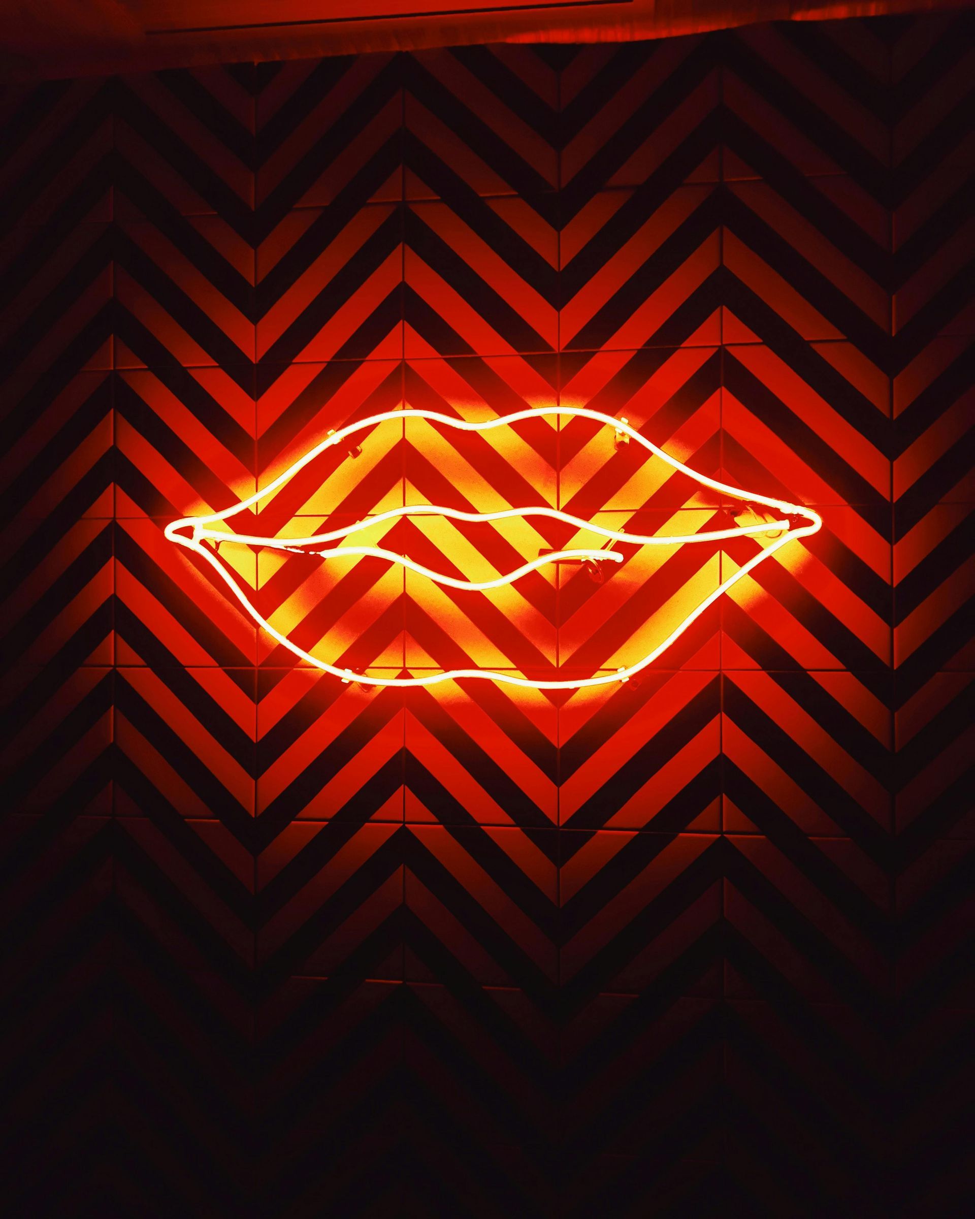 Neon orange lips on chevron red and black wall.