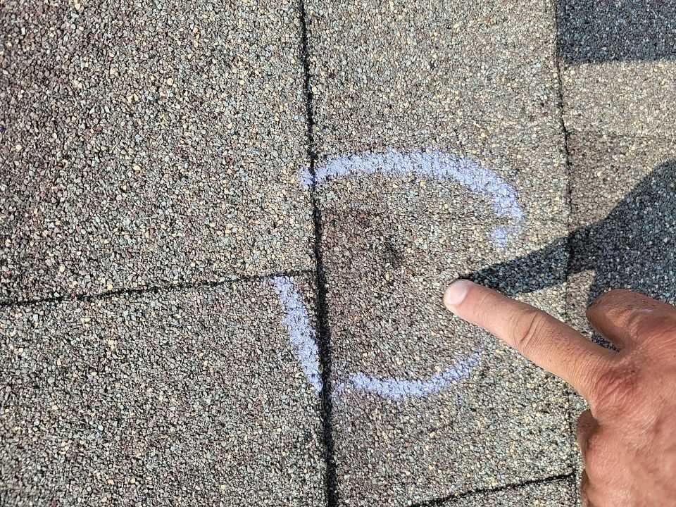 A person is pointing at a roof damage.