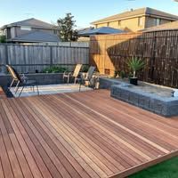 A wooden deck with chairs and a fire pit in a backyard.