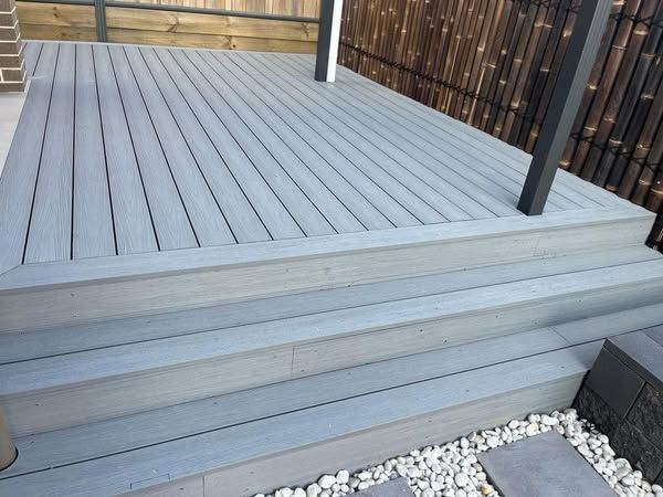 A gray deck with stairs and a fence in the background