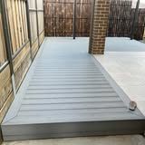 A gray deck with a brick wall and a fence in the background.