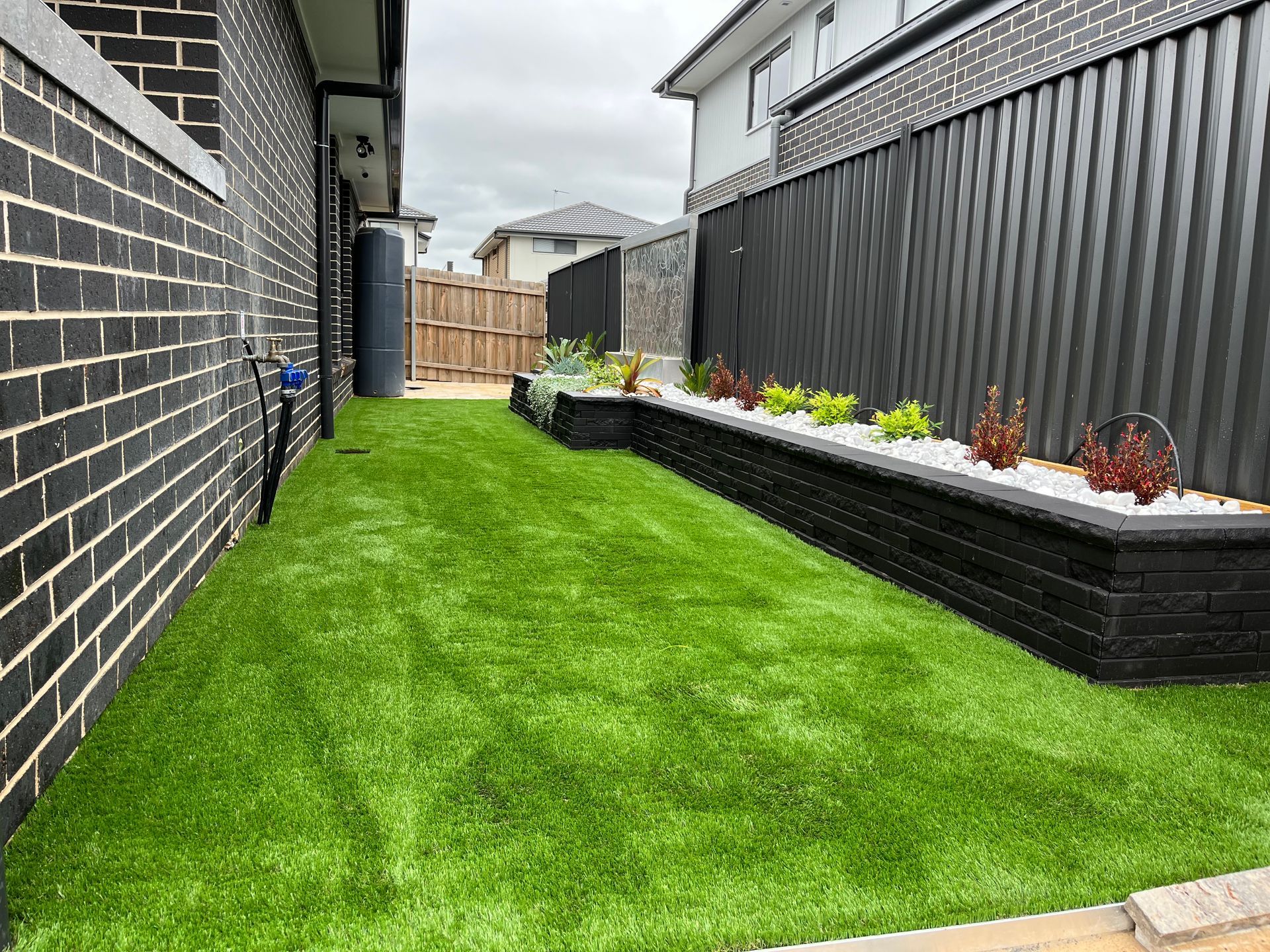 A lush green yard with a brick wall and a black fence.
